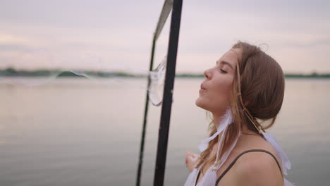 una joven artista sopla muchas burbujas de jabón muestra un espectáculo teatral usando un marco en cámara lenta al atardecer en un lago