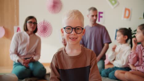 portrait of a happy preschool boy with white hair in glasses who looks at the camera and smiles against the background of his first lesson in preparation for school