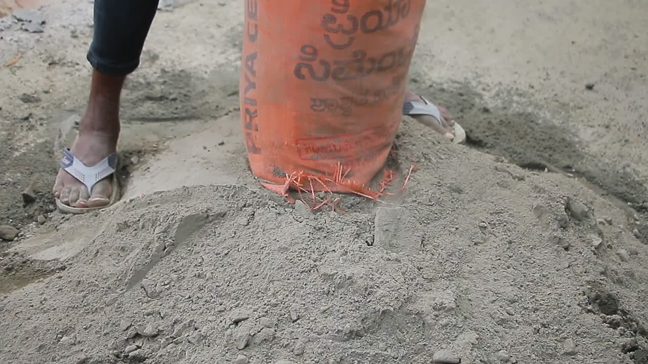 Mason worker dumping cement powder from a bag onto the ground at a construction site in Bangalore, India