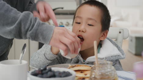 Lindo-Niño-Asiático-Comiendo-Gofres-Frescos-Para-El-Desayuno-Disfrutando-De-Una-Deliciosa-Comida-Casera-Con-La-Familia-En-La-Cocina-De-Casa-4k