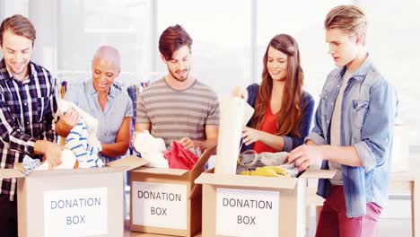 equipo ejecutivo creativo feliz clasificando ropa en la caja de donaciones