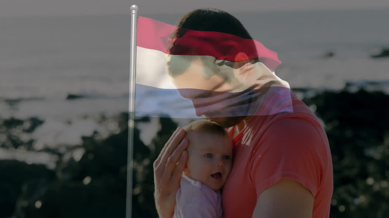 Holding baby, father with Netherlands flag overlay at rocky beach animation