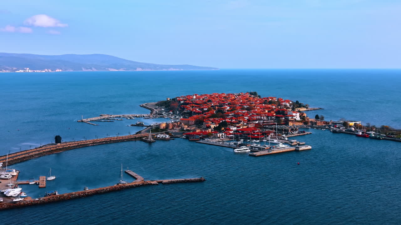 Vy av en kuststad ovanifrån med blått vatten och byggnader. Flygvy av en kuststad med röda tak, omgiven av blått vatten och en marina
