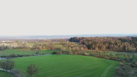 Aerial-panning-view-of-agricultural-field,-a-road-with-traffic,-a-valley,-and-backdrop-with-mountains-during-sunrise-in-Leimen,-Germany