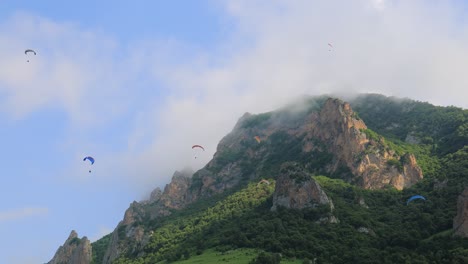 Paragliding-pilots-fly-paragliders-among-clouds-and-green-mountains.