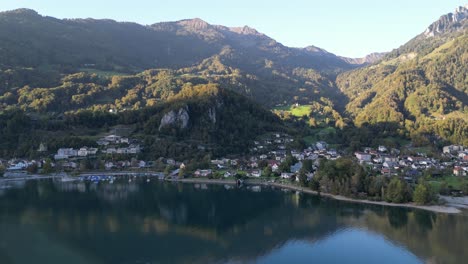 una vista aérea sobre walensee captura un pequeño puerto deportivo y casas residenciales con los majestuosos alpes de montaña vestidos de verde reflejados bellamente en el agua en un día soleado