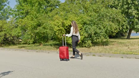 girl walking through green park in slow motion with red luggage, riga