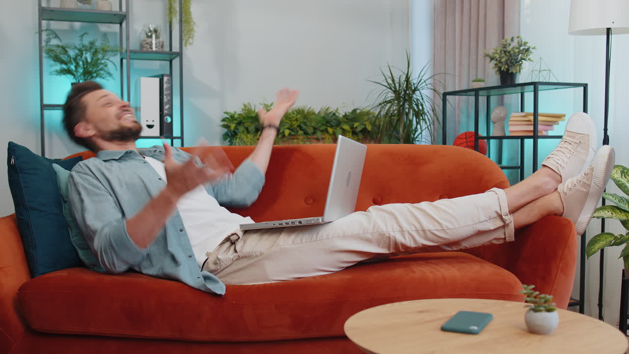 노트북에서 일하는 즐거운 젊은이가 성공을 축하하고 복권에서 돈을 벌고 온라인으로 좋은 소식을 얻습니다.