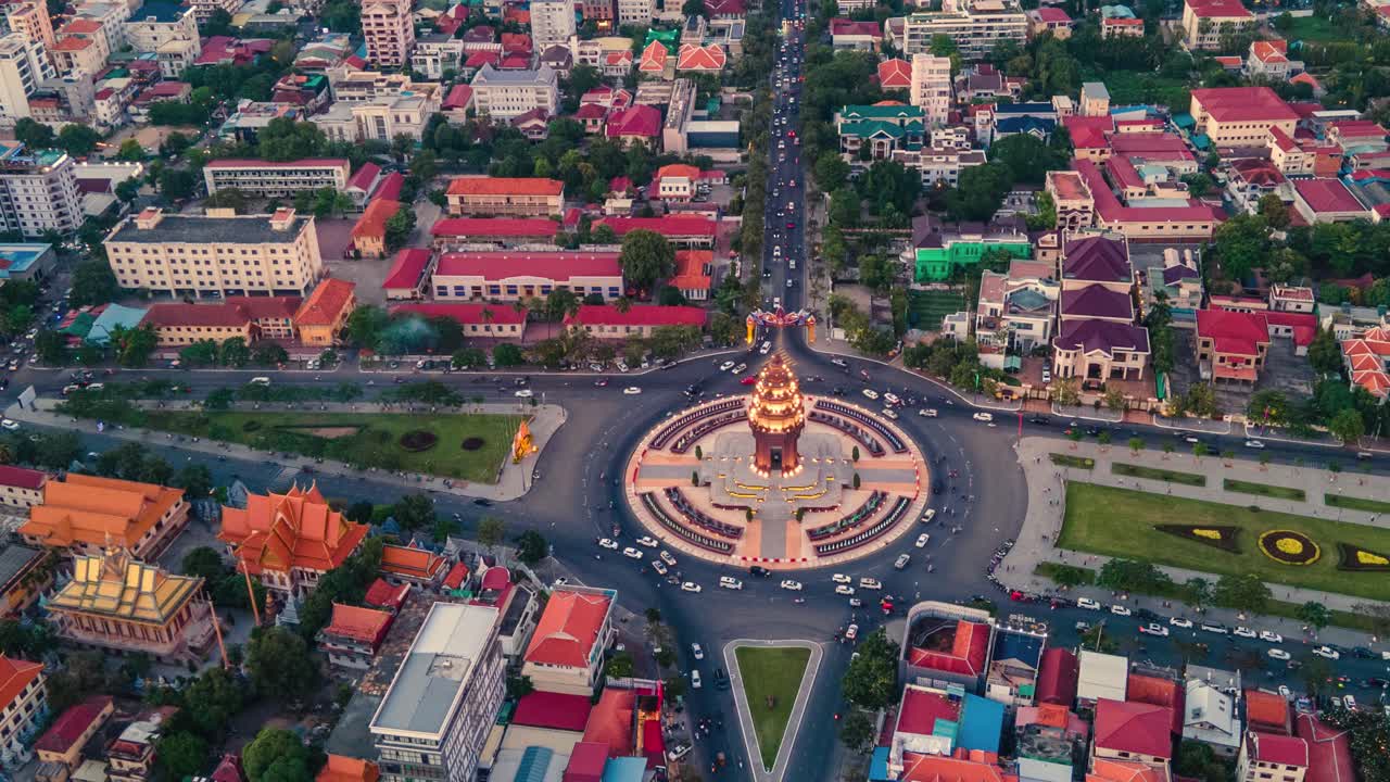 monumento a la independencia iluminado al atardecer con vehículos conduciendo en la intersección de norodom y sihanouk boulevard en phnom penh, camboya