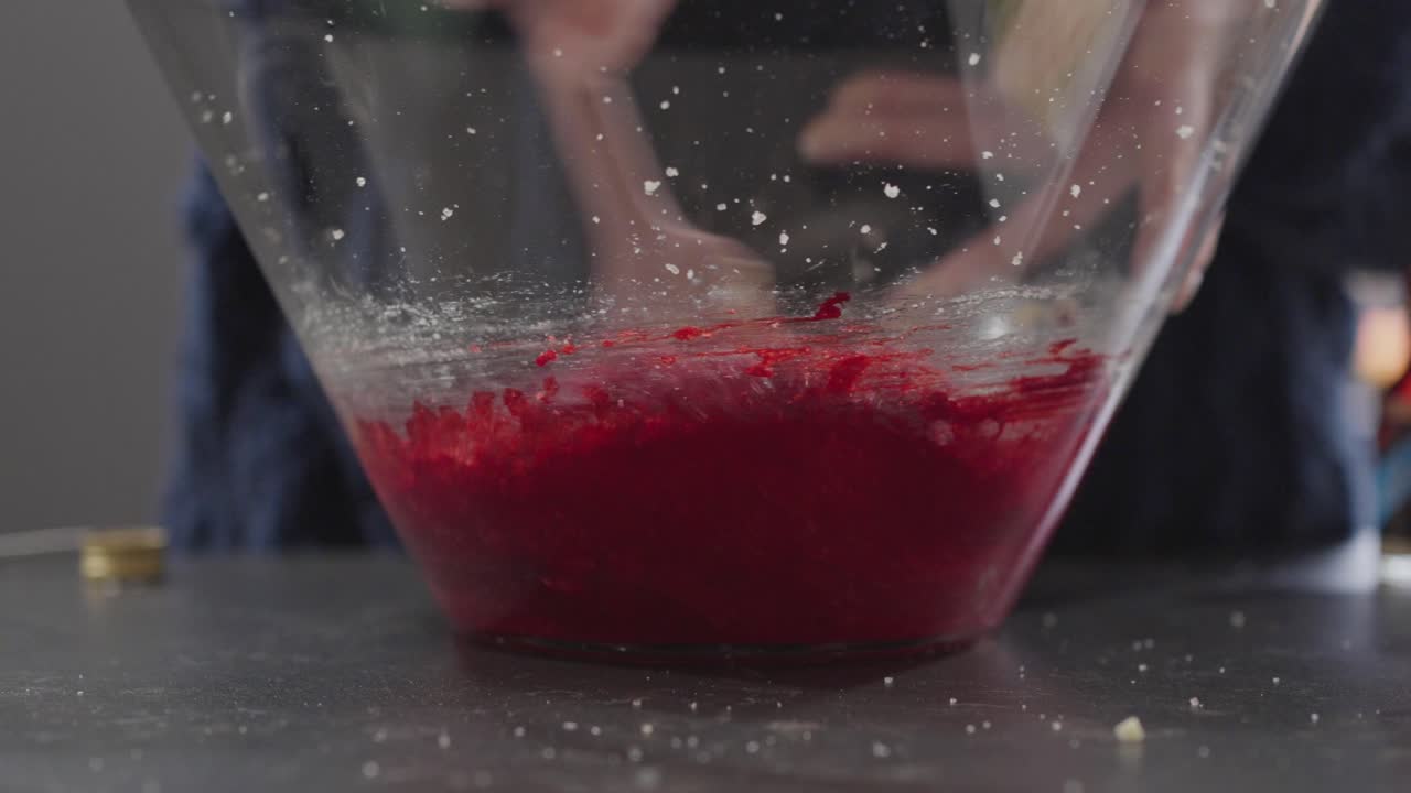 Hands kneading red velvet cookie dough inside glass bowl during preparation