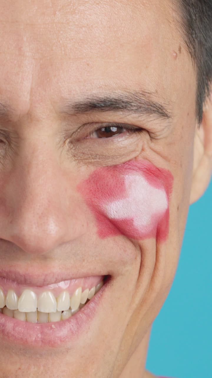 Uomo con una bandiera svizzera dipinta sul viso sorridente