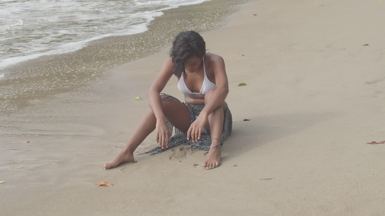 сексуальная девушка в бикини сидит на песке, прежде чем встать