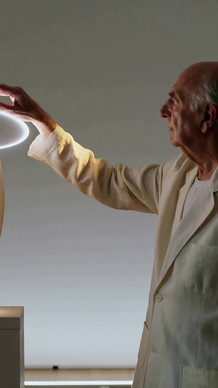Video verticale: Si vede un anello luminoso che raggiunge un anziano in cappotto beige che tocca un'aureola sopra un piedistallo.