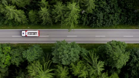 Tracking-a-big-lorry-driving-through-a-straight-street-in-a-forest,-aerial-following-shot-by-a-drone-in-4K