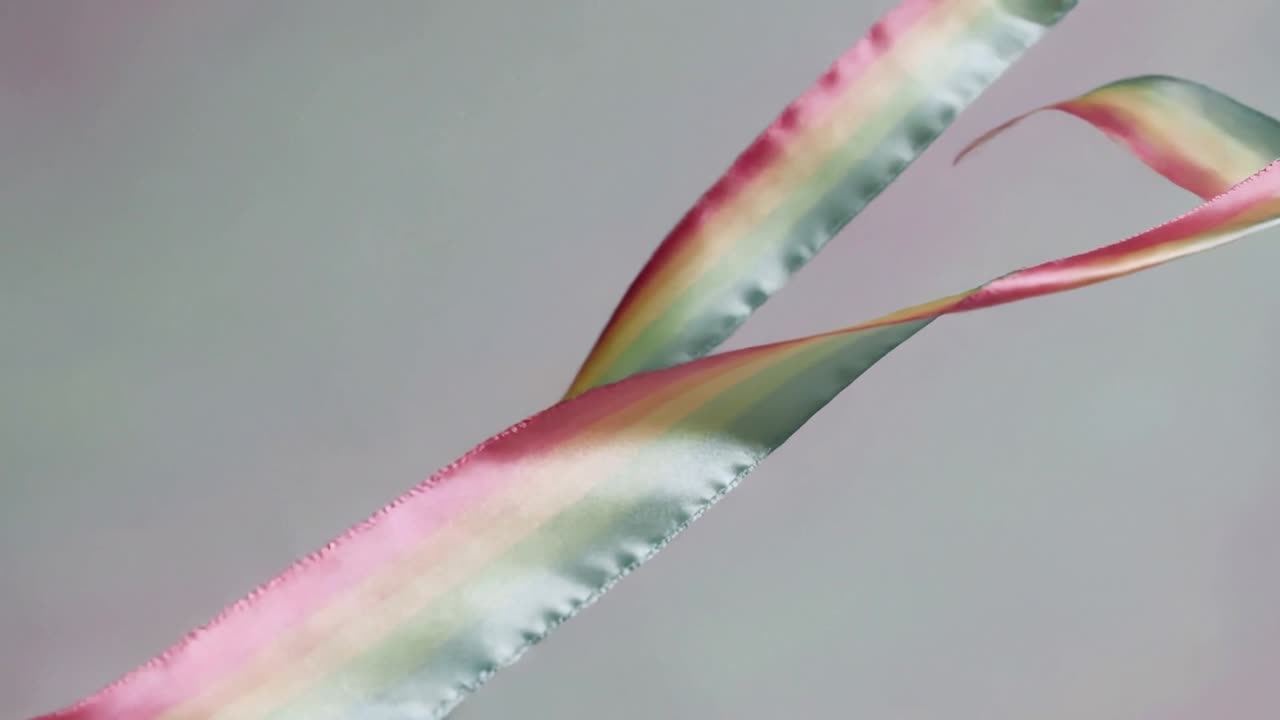 Un soffio del ventilatore fa attorcigliare, allentare e riallineare due nastri di raso attraverso lo studio con un arcobaleno.
