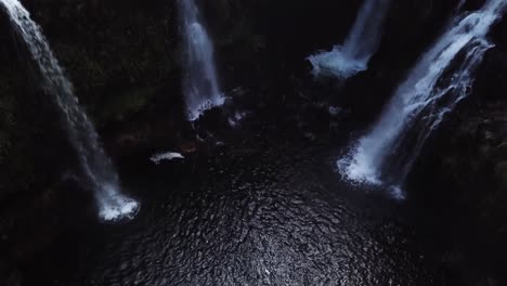 rising drone shot above a beautiful swimming hole with four gushing waterfalls pouring into it