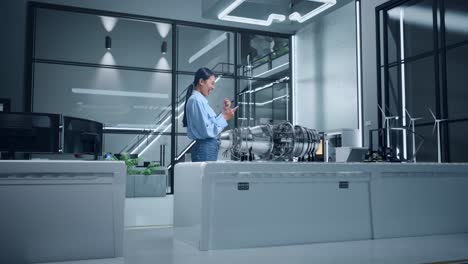 mujer ingeniera mirando un teléfono inteligente al lado de un modelo de motor de avión en una oficina moderna