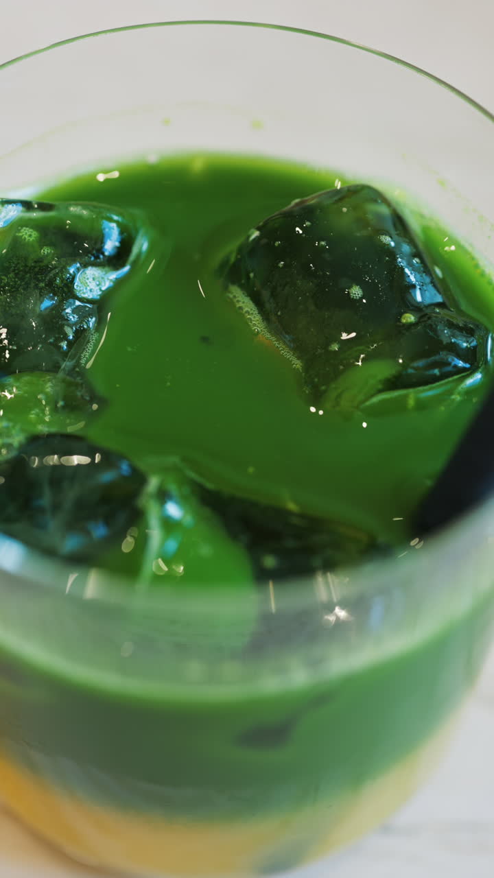 Close up of an iced matcha in a glass with a black straw at a cafe. Vertical