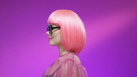 portrait of stylish woman wearing a pink wig and glamourous sunglasses turning face and smiling to the camera