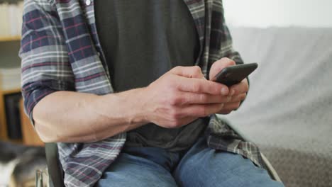 Happy-caucasian-disabled-man-in-wheelchair-using-smartphone-in-living-room