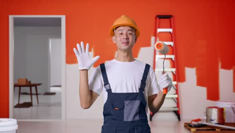 pintor hombre asiático con casco de seguridad sonriendo y diciendo wow mientras está de pie con la pared de pintura en la habitación