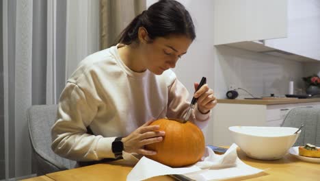 close up shot of a young woman carving orange pumpkin at home for the halloween