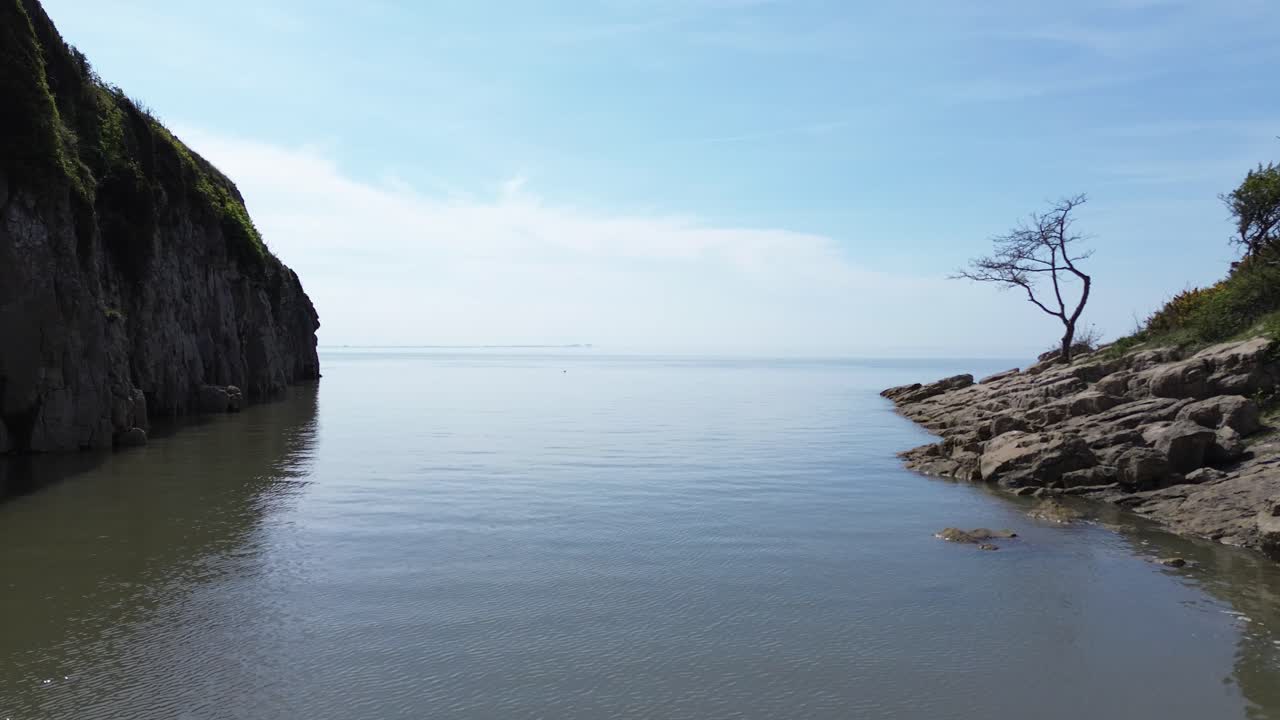 Idyllic rocky slope aerial view over calming tide and blue sky in dreamlike harmony paradise bay