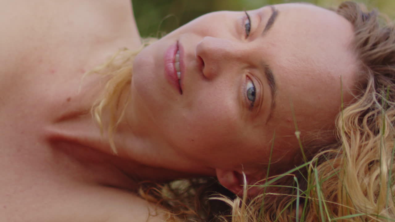 Close up of of a pretty woman lying down her head in the green grass on a sunny summer day