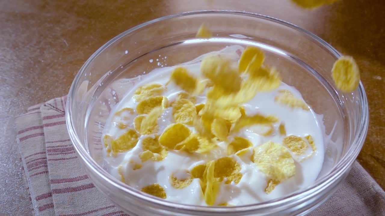 Knusprige gelbe Cornflakes in die Schale für ein köstliches Frühstück mit Milch am Morgen. Zeitlupe mit rotierender Kamerafahrt