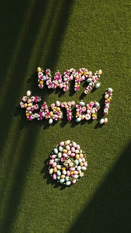 Top-down video shot of &#039;Happy Easter&#039; spelled with flowers and eggs on grass, capturing a festive