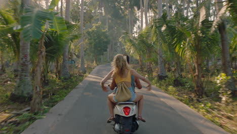 pareja feliz montando un scooter en una isla tropical novia divirtiéndose con los brazos levantados explorando un hermoso destino de viaje en motocicleta con su novio