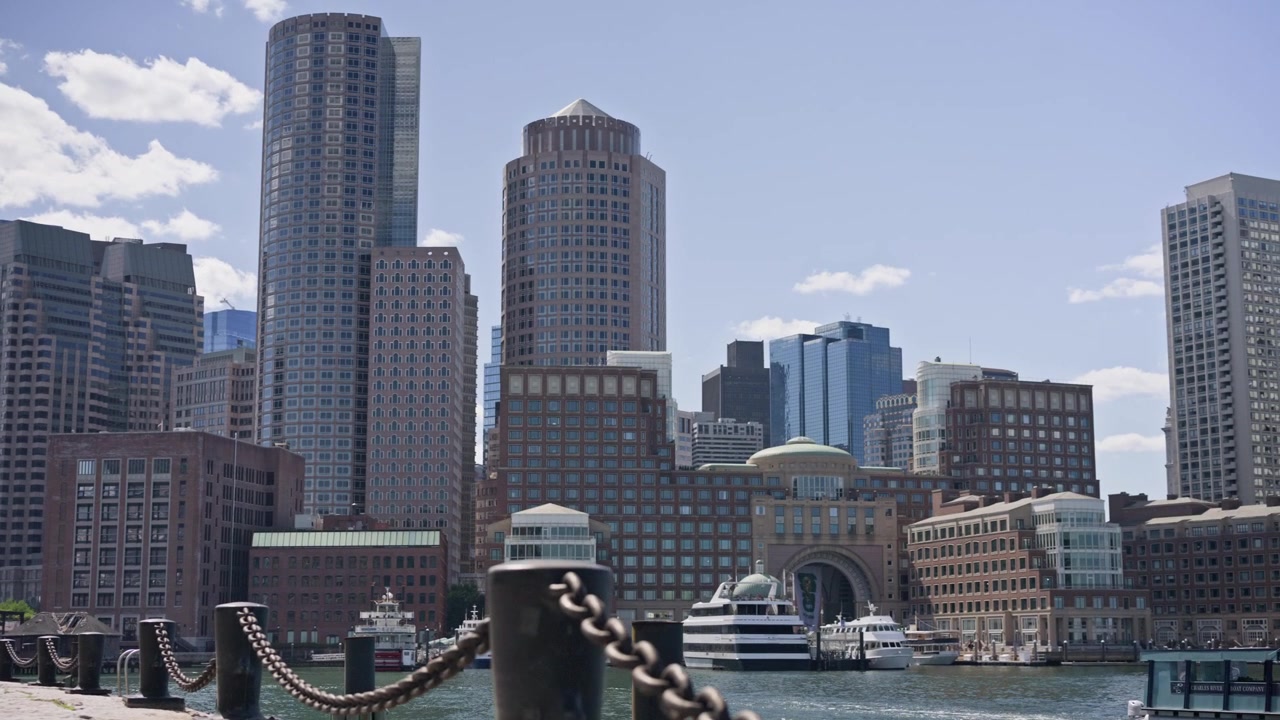 Ripresa cinematografica con dolly in alto e panoramica a destra attraverso il porto di Boston con una pesante catena portuale in primo piano che rivela lo skyline del centro di Boston. Sole splendente e vista scintillante sul lungomare