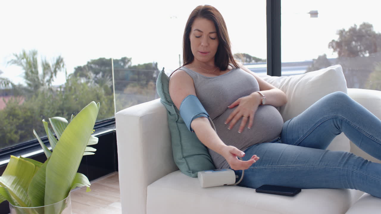 Checking blood pressure, pregnant woman sitting on couch, monitoring health