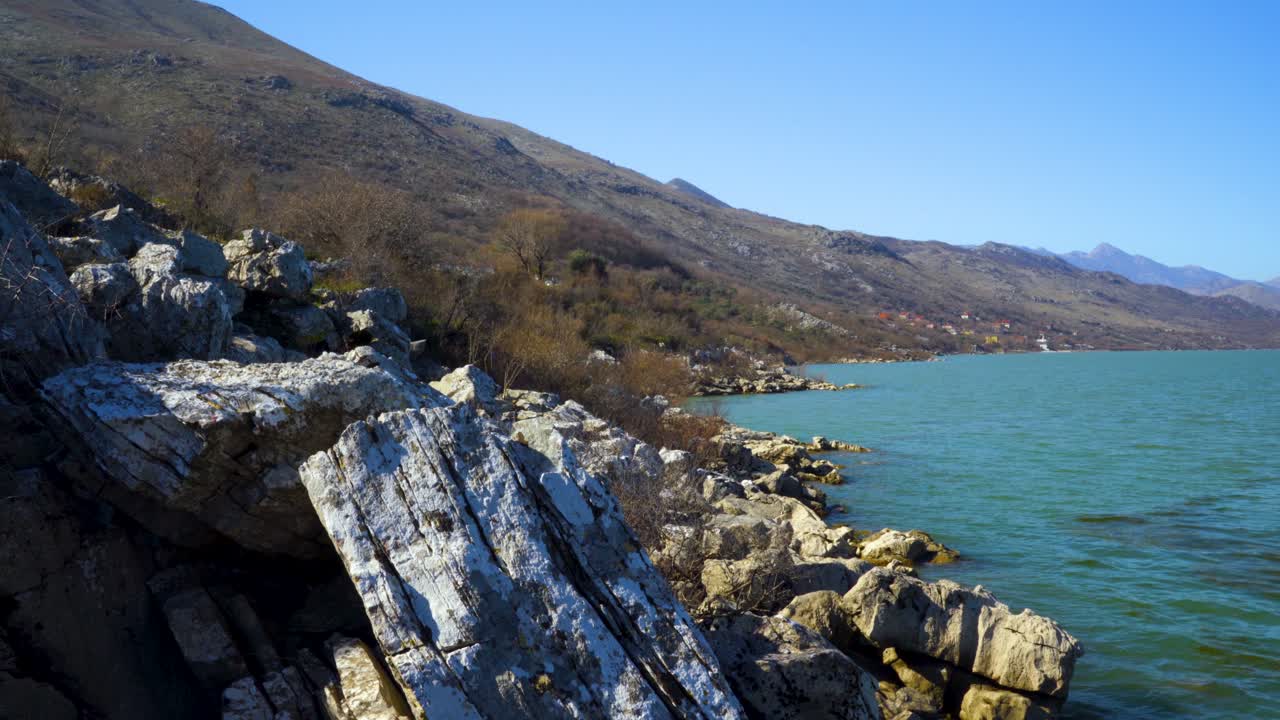 Big limestone cliffs on shore of lake with vibrant water, washing slopes of mountains with dry trees on winter