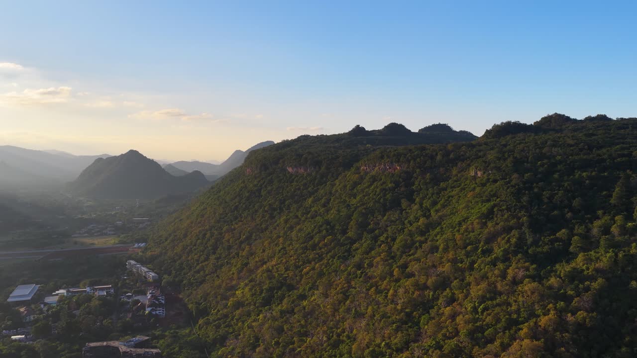 Filmagem feita com drone captura uma perspectiva aérea ampla de montanhas de floresta tropical sob céu azul claro