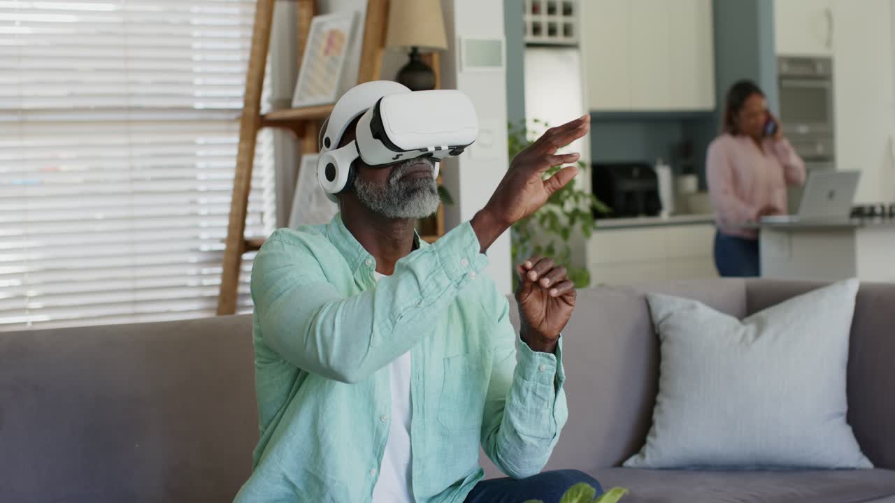Ældre par derhjemme, manden tager et hvidt VR-headset på for at manipulere virtuelle objekter nær en bærbar computer.