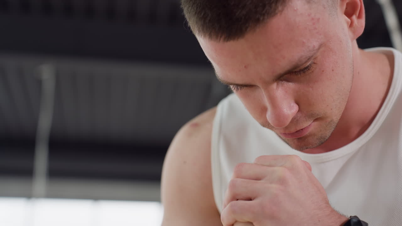 Close up of man with focused expression performing squat variation in modern gym studio with soft natural light and industrial ceiling design highlighting intensity and concentration during workout