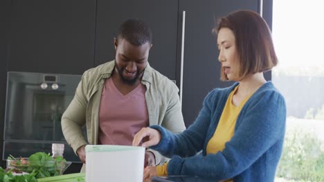 video of happy diverse couple preparing food and composting vegetable cuttings in kitchen