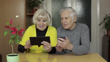 Pretty-mature-senior-couple-grandparents-enjoy-online-shopping-on-phone,-tablet