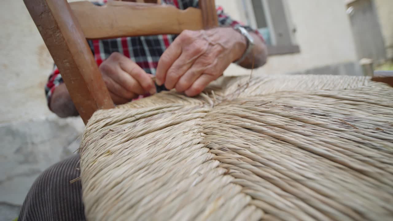 vista de primer plano cuando un hombre teje la parte sentada de una silla con su mano, italia.