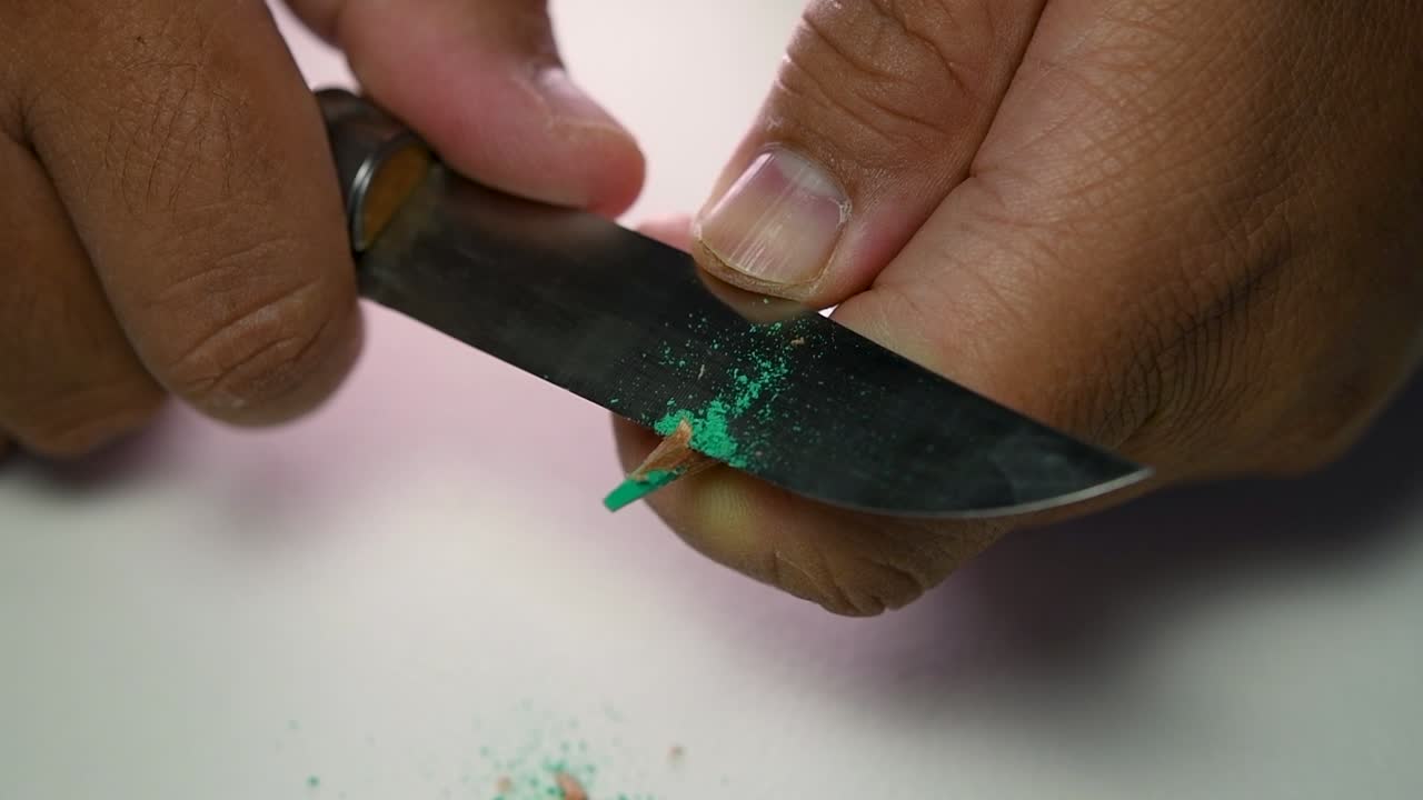 Footage of hands slowly sharpening a pencil and some coloured pencils with a sharp knife