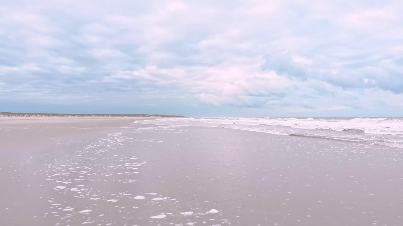 Drone shot of waves rolling onto a sandy beach, capturing the natural rhythm of the ocean