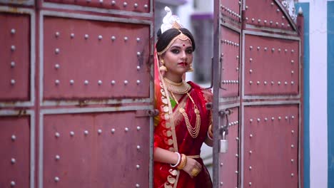 una novia india bengalí sonriente entra desde fuera de una gran puerta