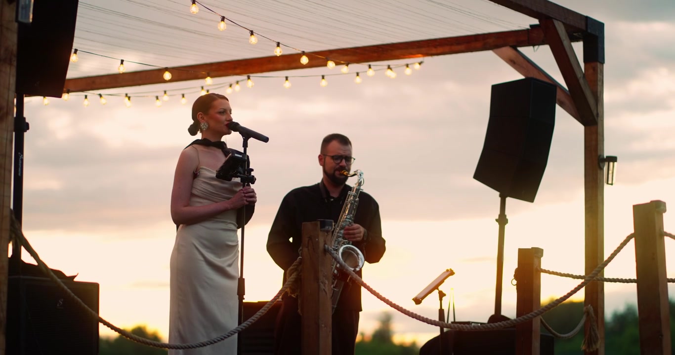 Kvindelig sanger og saxofonist optræder live på udendørs scene ved solnedgang