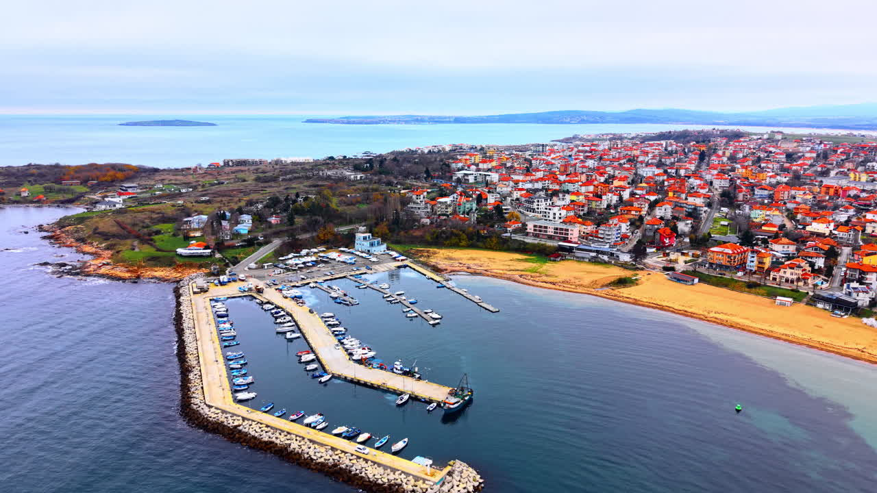 Kumlu bir plajın ve yerleşim bölgesinin yanında teknelerin ve yatların olduğu küçük bir liman. Limanın ve kıyı kasabası plajının havadan görünümü.