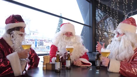 Friends in Santa Claus Costumes are Having Fun at a New Years Party Drinking Beer in a Pub Friends in Santa Claus Costumes are Having Fun at a New Years Party Drinking Beer in a Pub Close up