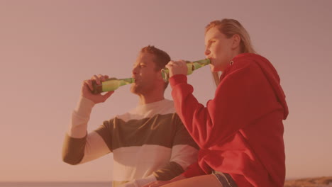 kaukasisch stel dat samen op het strand toast en bier drinkt.