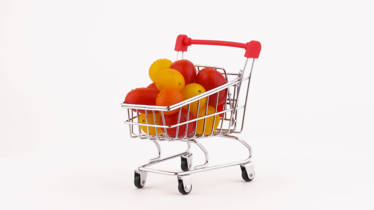 빨간색과 노란색 포도 토마토로 가득 찬 쇼핑 카트는 물방울로 쌓여 있습니다. 회전 테이블에 회전합니다. 색 배경에 고립되어 있습니다. 근접.