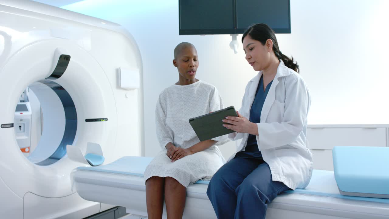 Una tecnica donna e una paziente afroamericana che esaminano un tablet vicino al gantry della TC, preparandosi per la tomografia computerizzata.