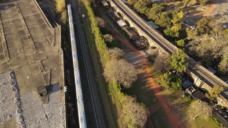 impresionante vista aérea de un tren moderno que se mueve a lo largo de las vías en medio de un área urbana al atardecer